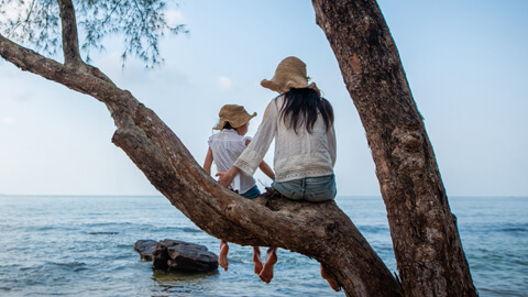 Mother and daughter sitting in tree overlooking ocean